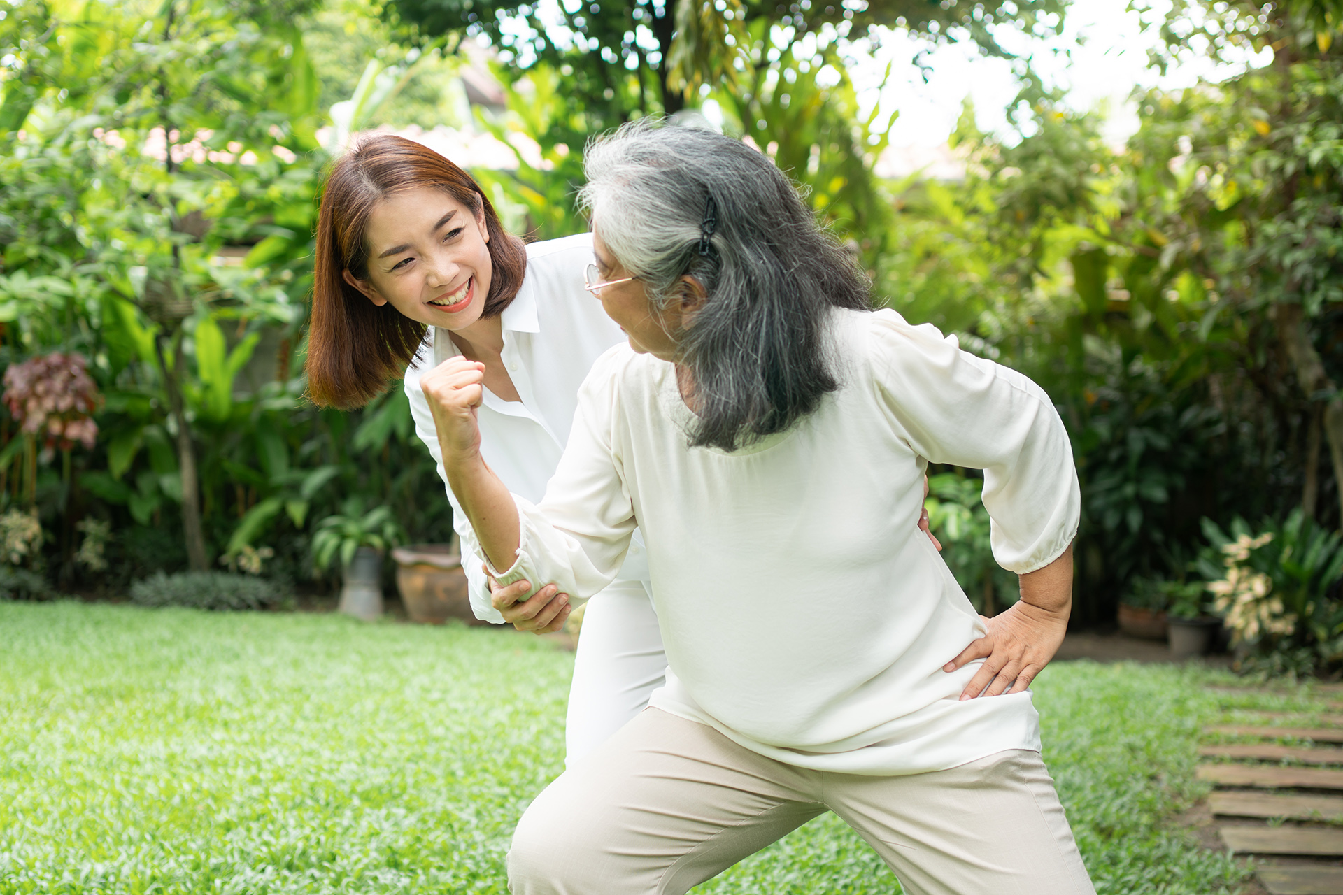 An old elderly Asian woman and exercise in the backyard with her daughter.  Concept of happy retirement With care from a caregiver and Savings and senior health insurance, Happy family