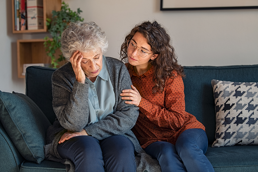 Caring daughter comforting frustrated unhappy senior woman. Loving adult granddaughter talking to sad old grandmother and comforting her. Upset widowed woman with headache consoled by her daughter.